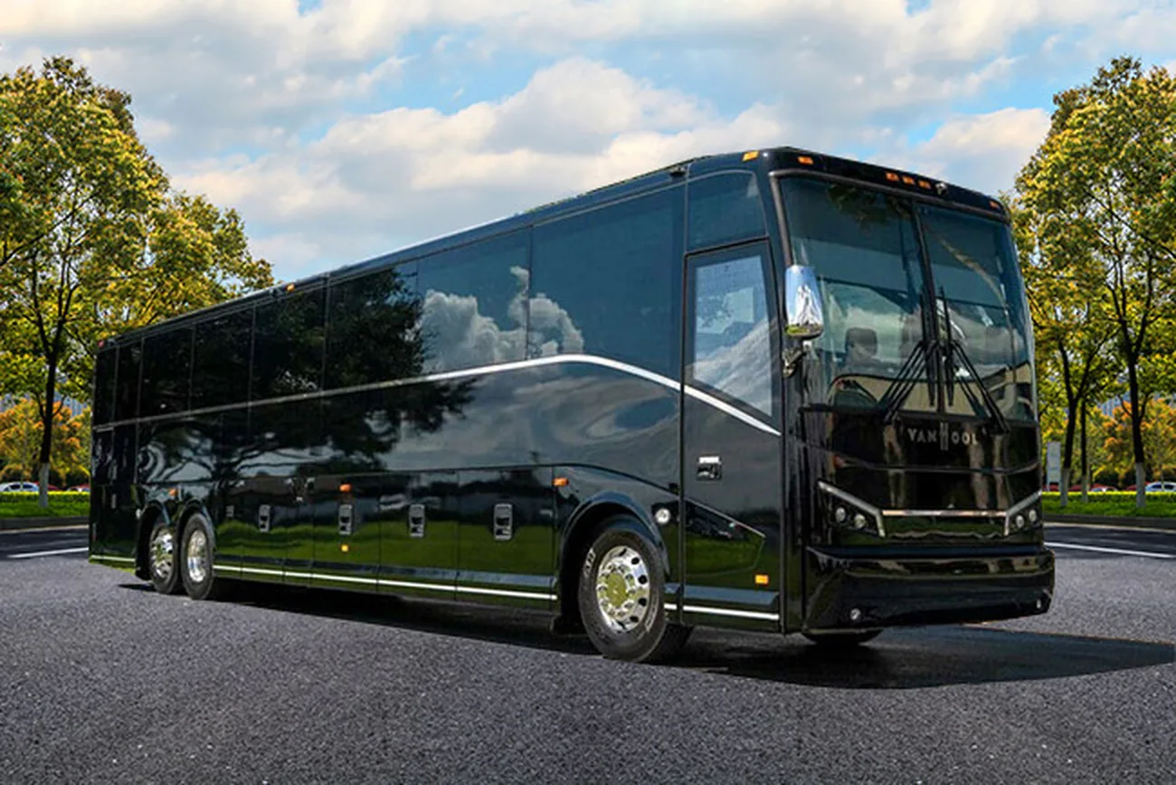 A black 56-passenger Van Hool motor coach parked in a tree-lined parking area.